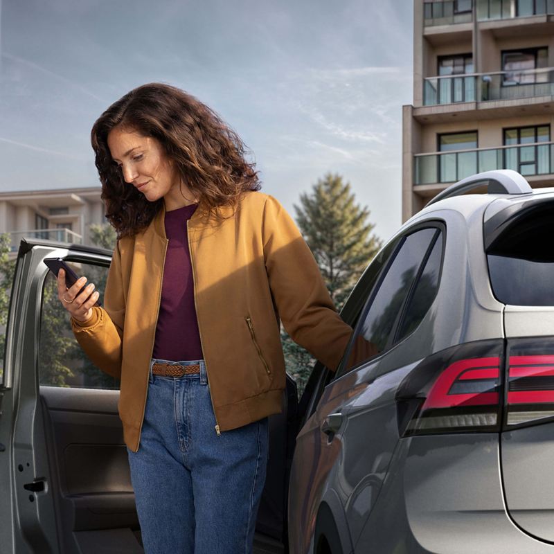 A woman holding a phone whilst standing by an opened car door