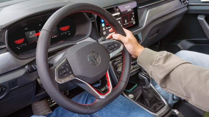 Interior frontal de Volkswagen Taigun con volante negro y manos del conductor, visto de lado.