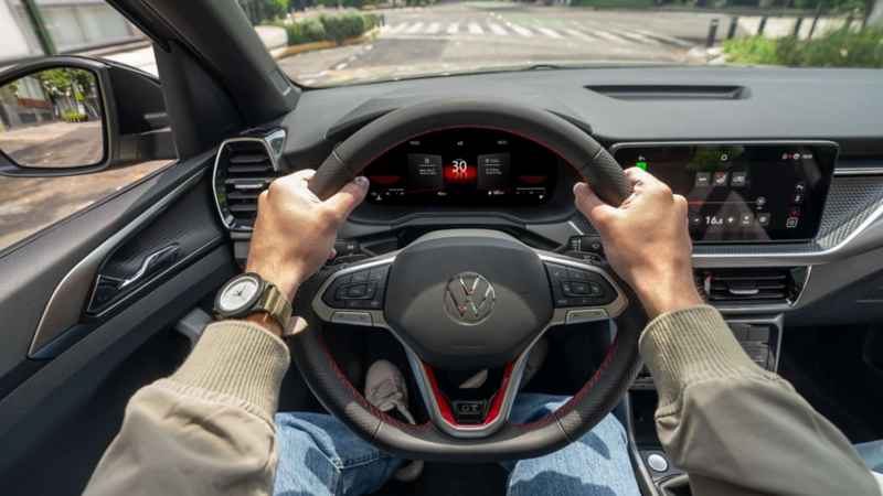Vista de conducción de Volkswagen Taigun con volante negro, pantalla digital y manos del conductor.