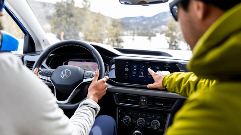 Une personne conduit un VWUS Taos 2022 de Volkswagen tandis qu’un homme touche l'écran d'infodivertissement.