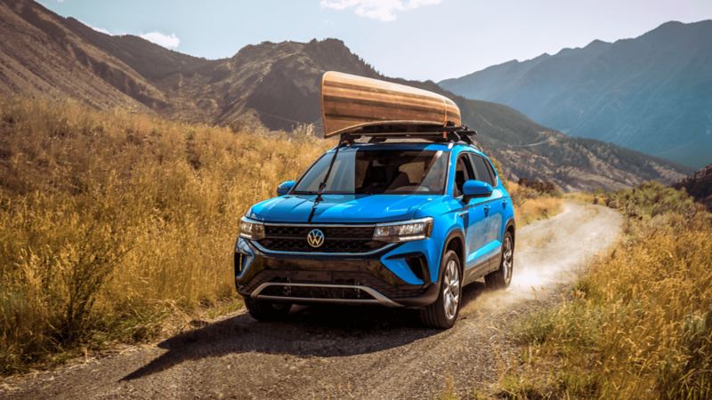 A Cornflower Blue 2022 Volkswagen Taos SUV with a canoe attached to the roof driving on a mountain road.