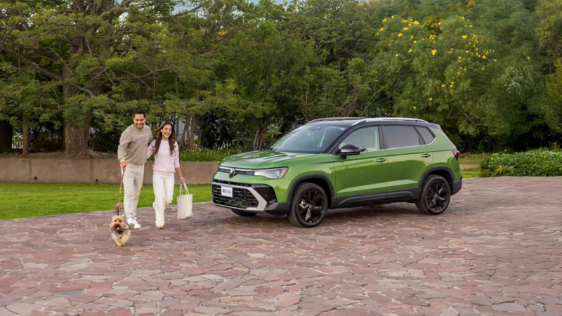 Camioneta Taos de color verde con pareja y perrito que caminan frente a SUV. 