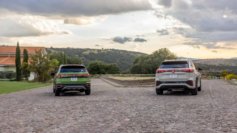 SUV Taos de color verde y Tiguan de color gris. Vista trasera de vehículos en camino empedrado.