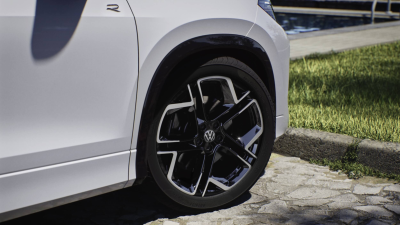 Close-up of a white Volkswagen Tayron's rear wheel with a sleek, modern alloy design, parked on a cobblestone surface next to well-manicured grass, conveying elegance.