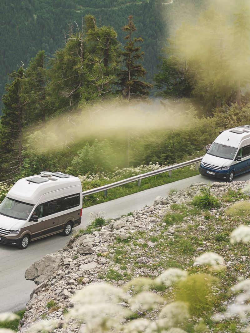 Zwei Grand California von VW fahren durch eine Berglandschaft.