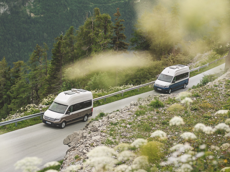 Zwei Grand California von VW fahren durch eine Berglandschaft.