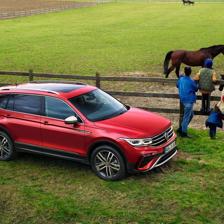 Un chico con un caballo delante de un SUV rojo de Volkswagen