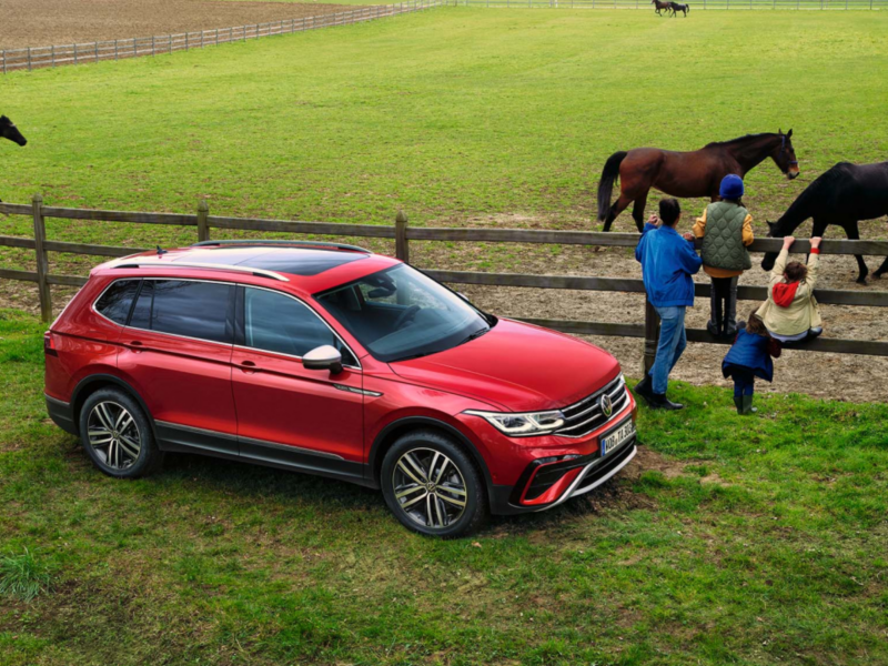 Un chico con un caballo delante de un SUV rojo de Volkswagen