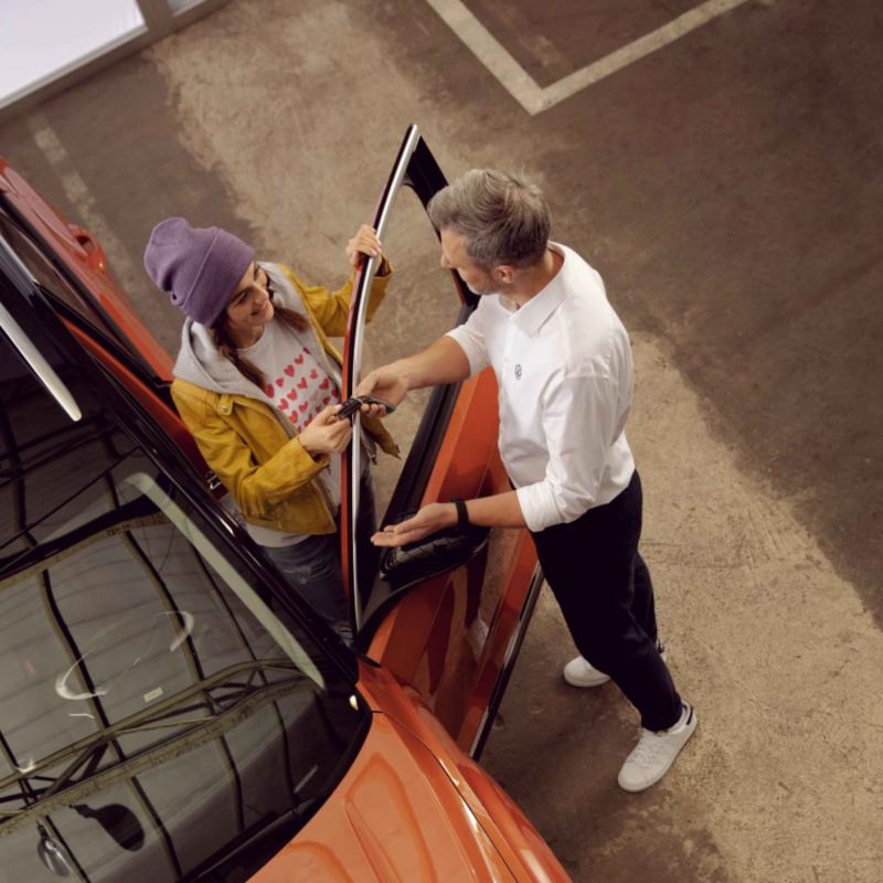 Agente de servicio de Volkswagen con una chica de pie junto a un Volkswagen naranja
