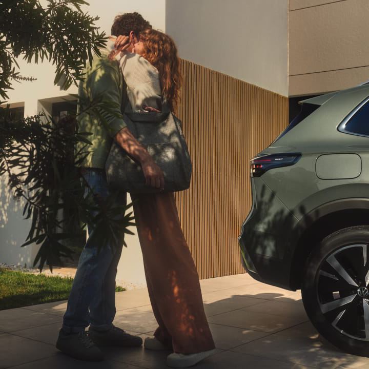 Una pareja abrazándose junto a un Volkswagen aparcado en casa