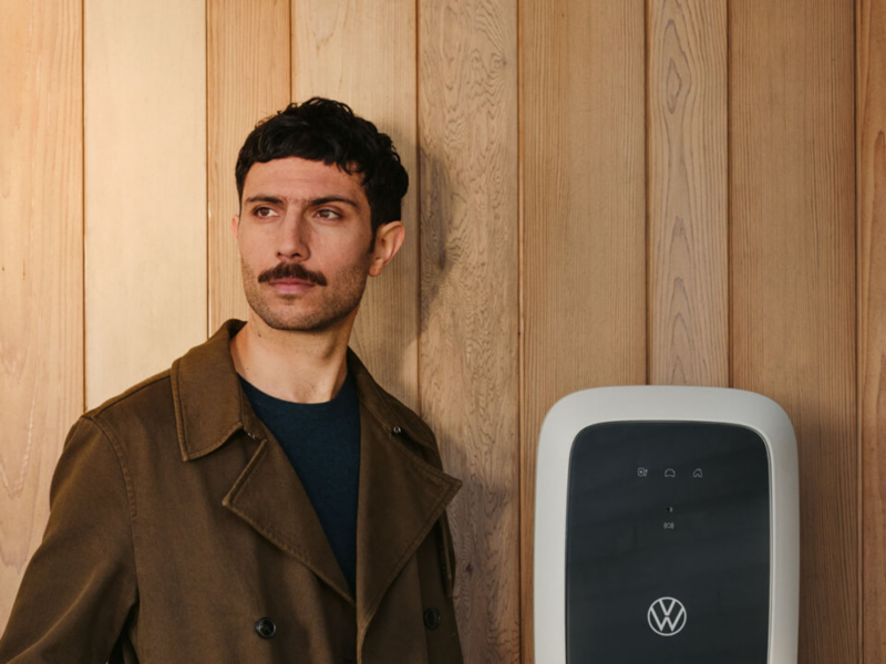 Chico con los brazos cruzados mirando a la cámara apoyada sobre una pared ocre con un ID.Charger de Volkswagen