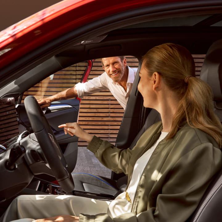 Una mujer sentada al volante de un Volkswagen nuevo de stock y un agente de pie fuera del coche