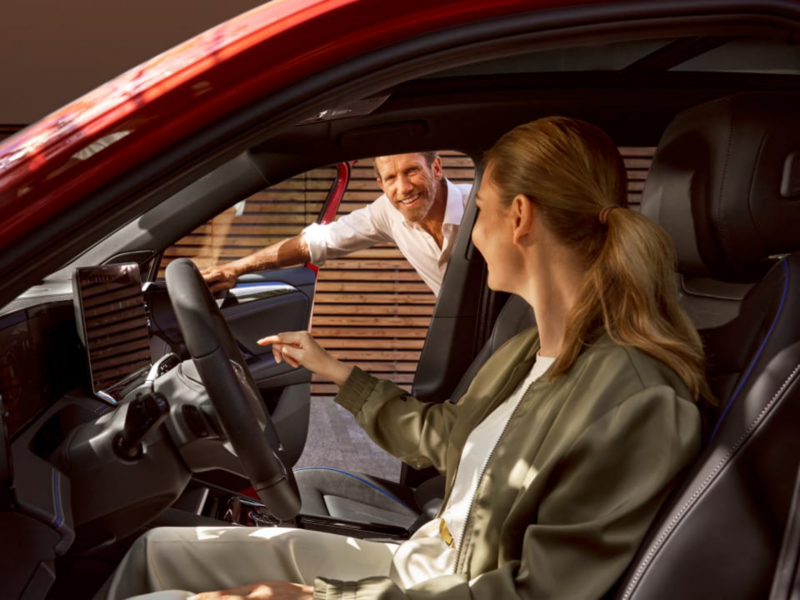 Una mujer sentada al volante de un Volkswagen nuevo de stock y un agente de pie fuera del coche