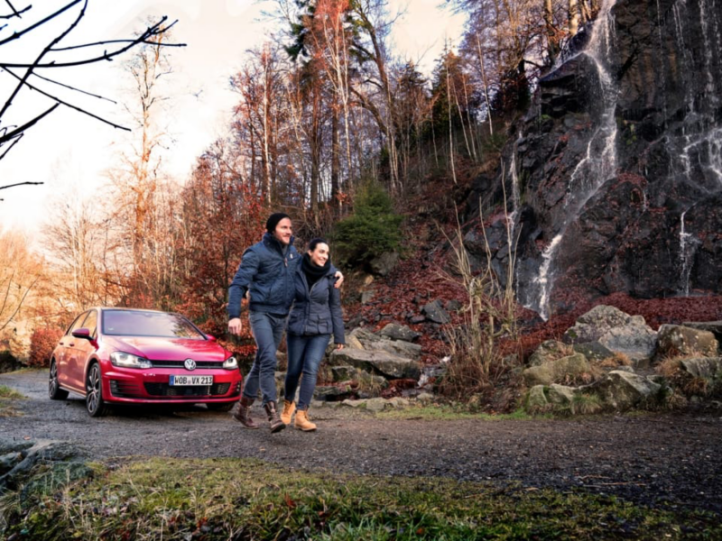 Una pareja al lado de un Volkswagen de color rojo estacionado en la montaña