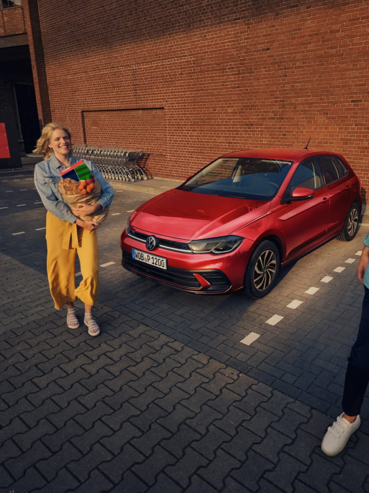 Una mujer junto un Volkswagen rojo