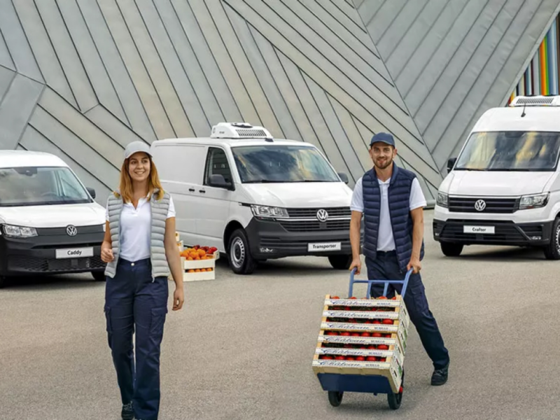 Un hombre con una carreta y una mujer delante de las unas furgonetas Volkswagen blancas