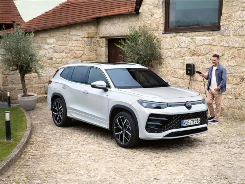 Un Volkswagen de color blanco estacionado fuera de una carga junto a un hombre con un cargador en la mano