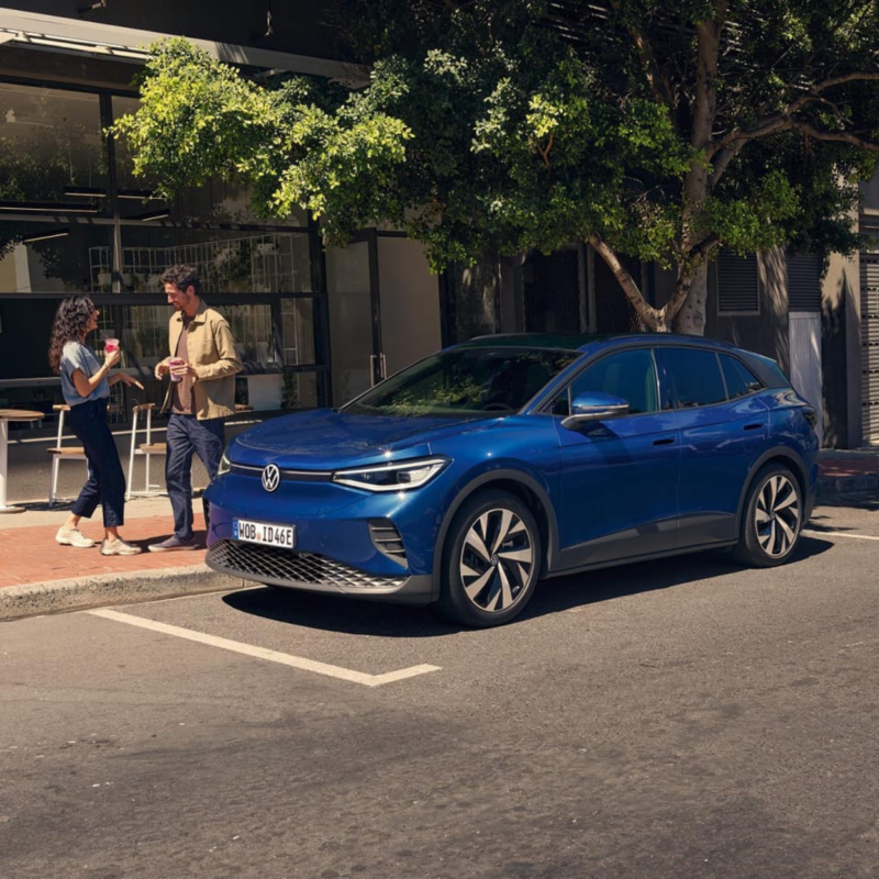 Dos chicos al lado de un Volkswagen eléctrico de color azul oscuro estacionado en la calle