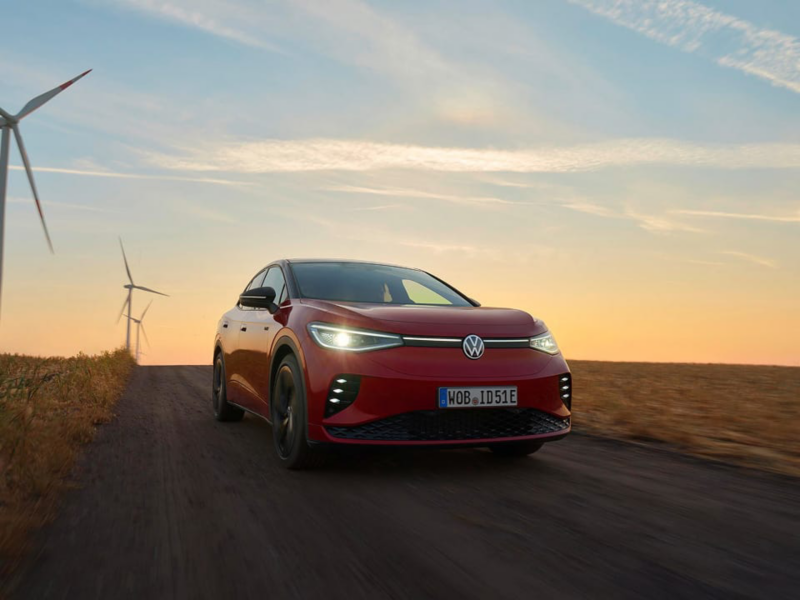 Un Volkswagen ID. rojo al atardecer junto a unos aerogeneradores