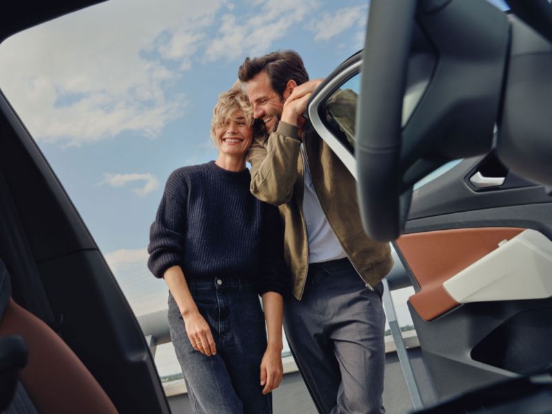 Una pareja sonriendo vistos desde el interior de un Volkswagen con la puerta abierta