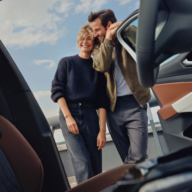 Una pareja sonriendo vistos desde el interior de un Volkswagen con la puerta abierta