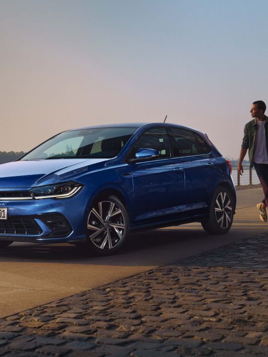 Un chico caminando hacia un Volkswagen Polo aparcado en un malecón