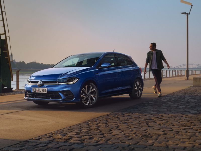 Un chico caminando hacia un Volkswagen Polo aparcado en un malecón