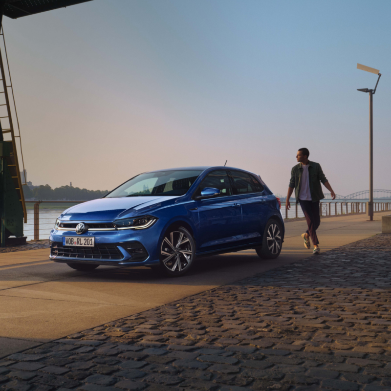 Un chico caminando hacia un Volkswagen Polo aparcado en un malecón