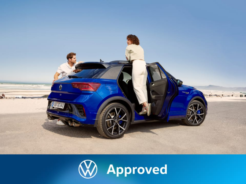 Una pareja junto a un Volkswagen T-Roc azul en la playa