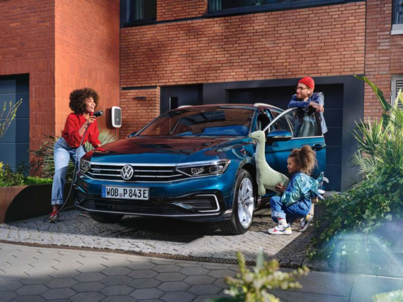 Familia junto a un Volkswagen Passat híbrido enchufable azul aparcado en casa