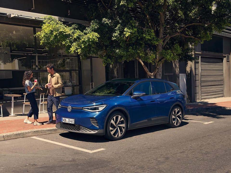 Dos personas en la calle con su vehículo eléctrico de Volkswagen aparcado al sol