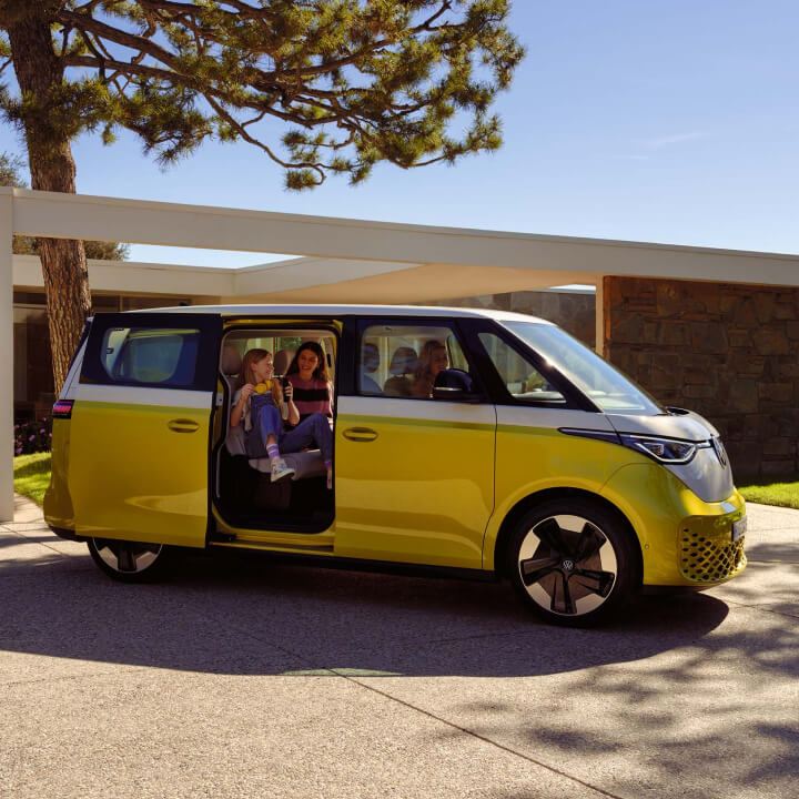 Una familia con Volkswagen ID. Buzz bicolor aparcado delante de casa