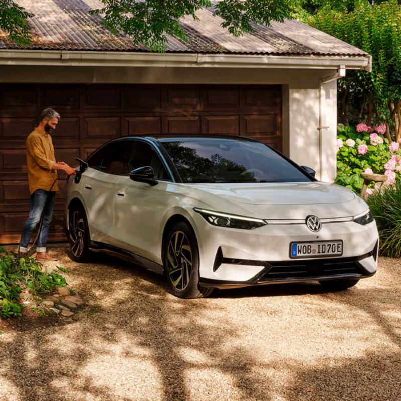 Un hombre junto a un Volkswagen ID.7 de color blanco estacionado delante de una casa