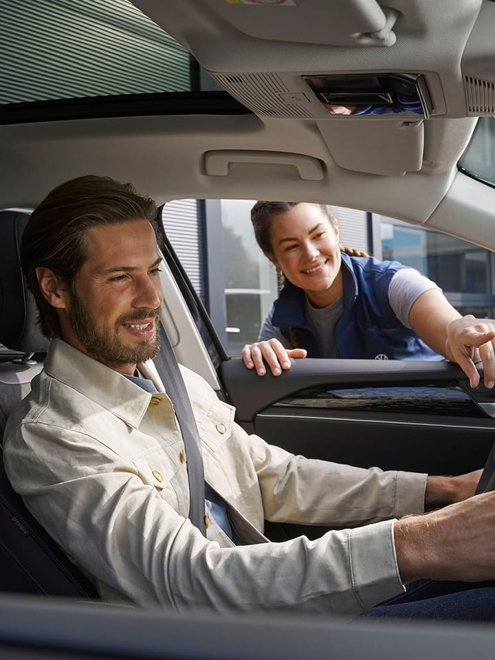 Un hombre dentro de un Volkswagen y una mujer del servicio técnico ayudandole