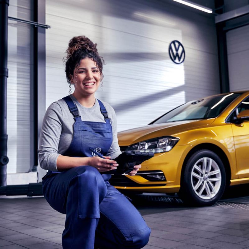 Una trabajadora de Volkswagen delante de un Volkswagen en un taller