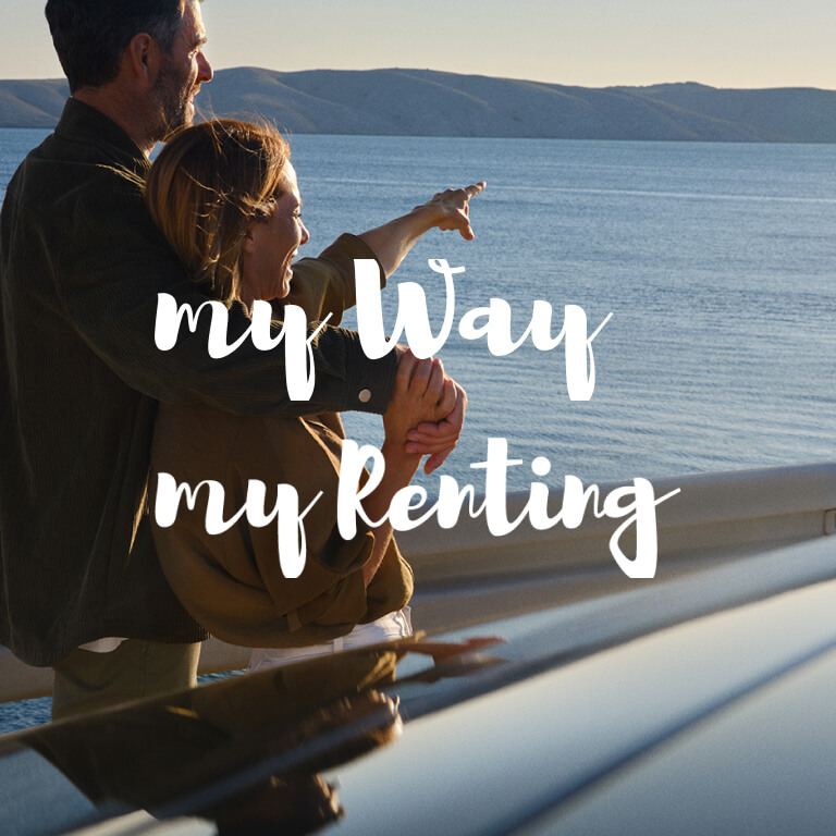 Una pareja sentada en un bordillo delante de un Volkswagen con los logos de My Way y My Renting