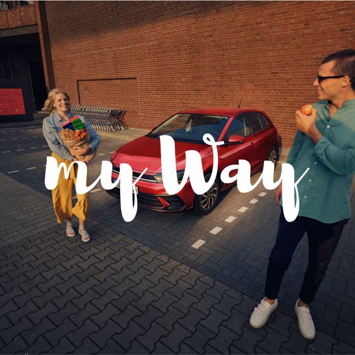 Una pareja saliendo del supermercado delante de un Volkswagen con el logo de My Way
