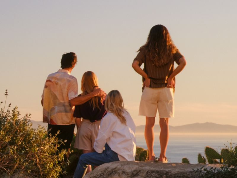 Vier Personen von hinten zu sehen stehen an einer Klippe und schauen in den Sonnenuntergang