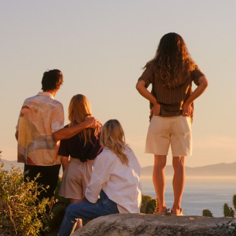Vier Personen von hinten zu sehen stehen an einer Klippe und schauen in den Sonnenuntergang