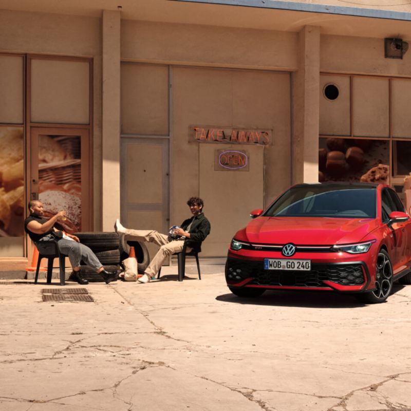 Una pareja sentada delante de un Volkswagen Golf 8 GTI rojo