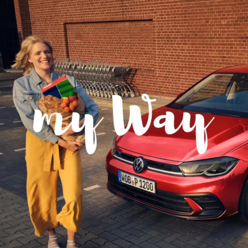 Una chica al lado de un Volkswagen rojo con el logo My Way