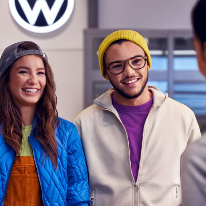 Una pareja sonriendo hablando con una agente en un concesionario de Volkswagen