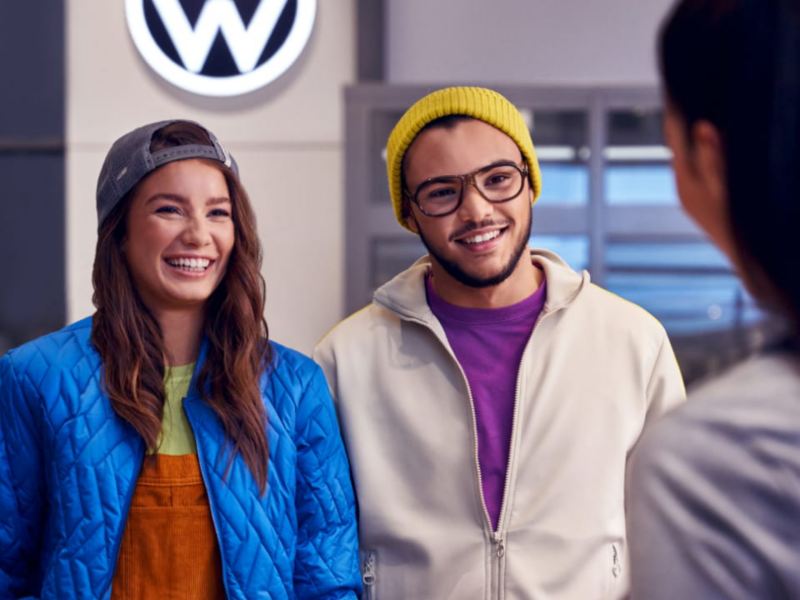 Una pareja sonriendo hablando con una agente en un concesionario de Volkswagen