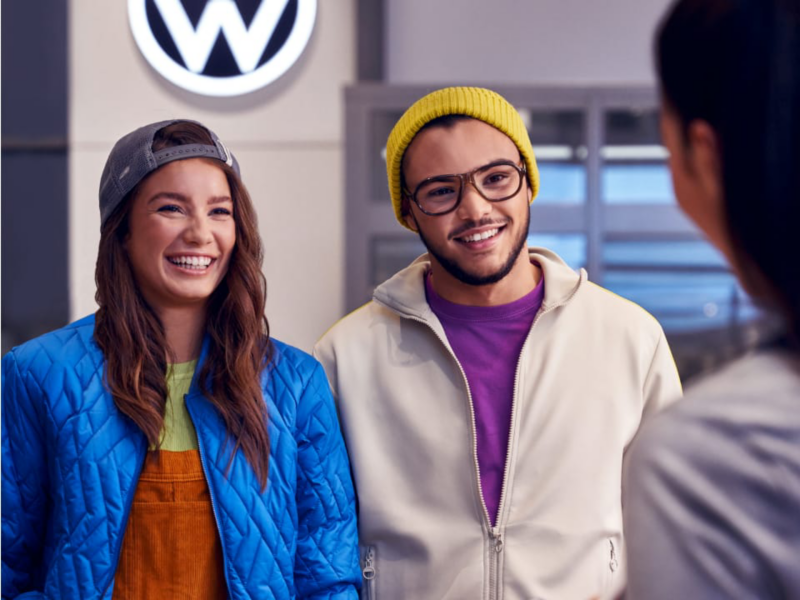 Una pareja sonriendo hablando con una agente en un concesionario de Volkswagen