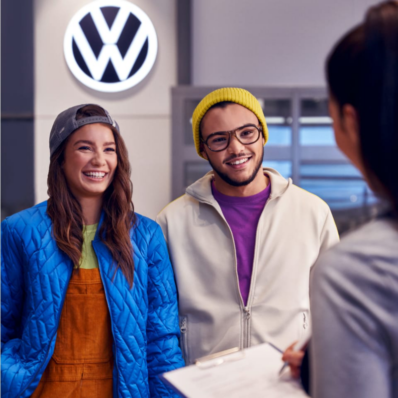 Una pareja sonriendo hablando con una agente en un concesionario de Volkswagen