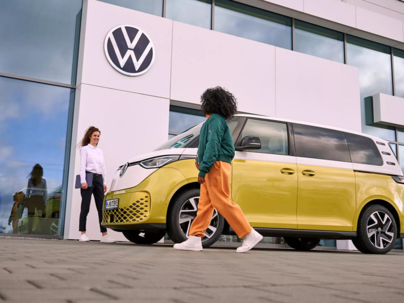 Dos personas con una Volkswagen ID. Buzz bicolor frente a un consesionario