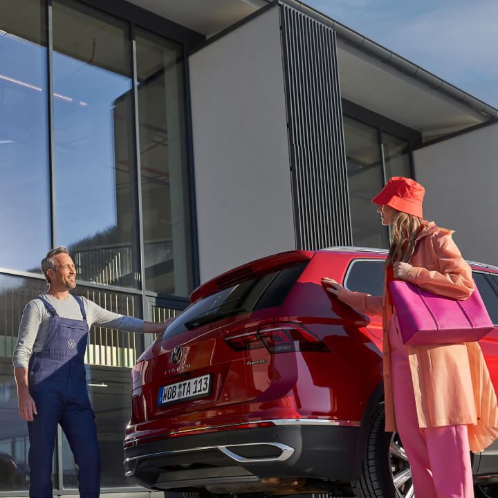 Un agente de servicio y una clienta junto a un Volkswagen rojo en un concesionario