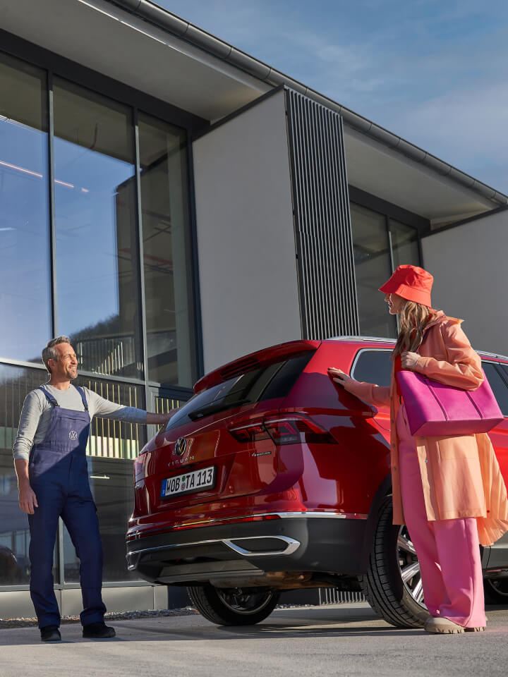 Un agente de servicio y una clienta junto a un Volkswagen rojo en un concesionario