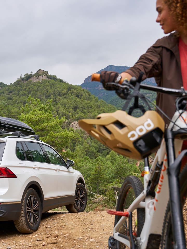 Una chica con una bicicleta en la montaña junto a un Volkswagen de Rent-a-Car