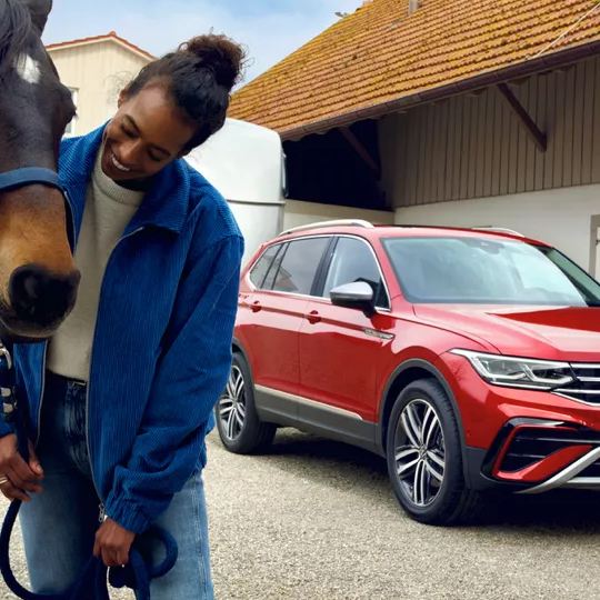 Un chico con un caballo y un Volkswagen SUV rojo al fondo